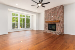 A living space from Compass Homes Ohio with a brick fireplace, large windows, and hardwood floors.
